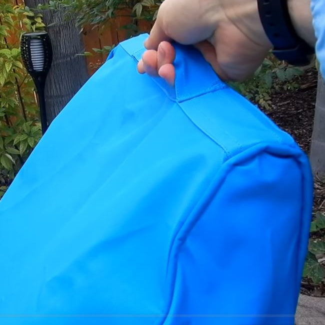Hand gripping the top carry handle on the blue Riptide pool vacuum system cover
