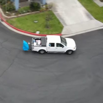 Aerial view of white pickup truck towing Riptide pool vacuum system with blue cover secured on trailer